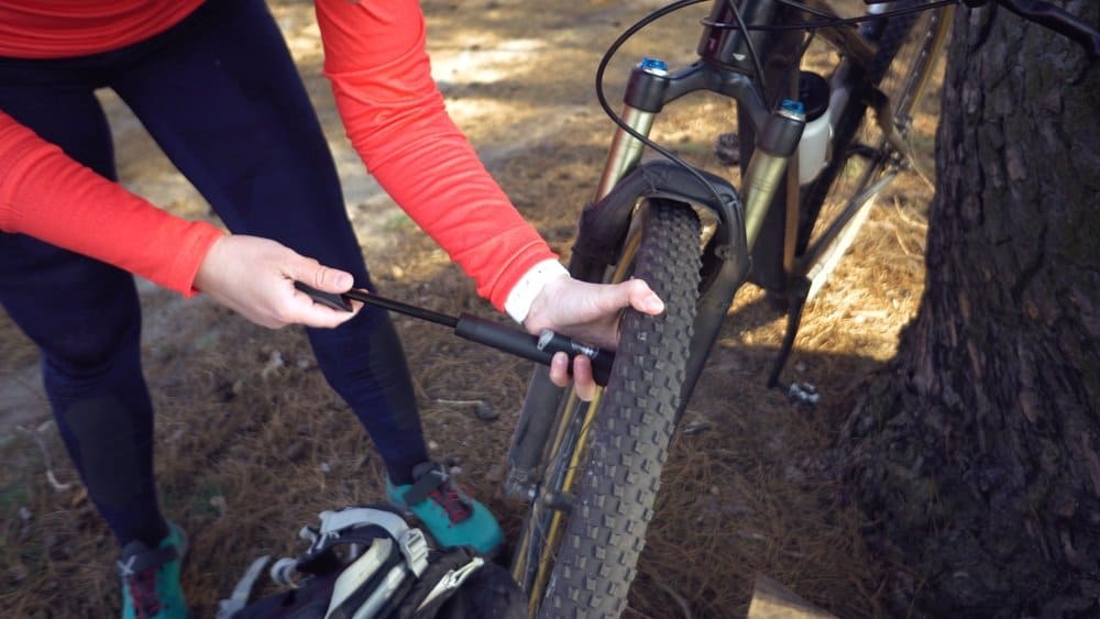 Young caucasian woman athlete tourist cyclist uses a hand tool, a bicycle pump to inflate air into a tire wheel mountain bike. Breakdown and quick repair of a bicycle in the countryside outside